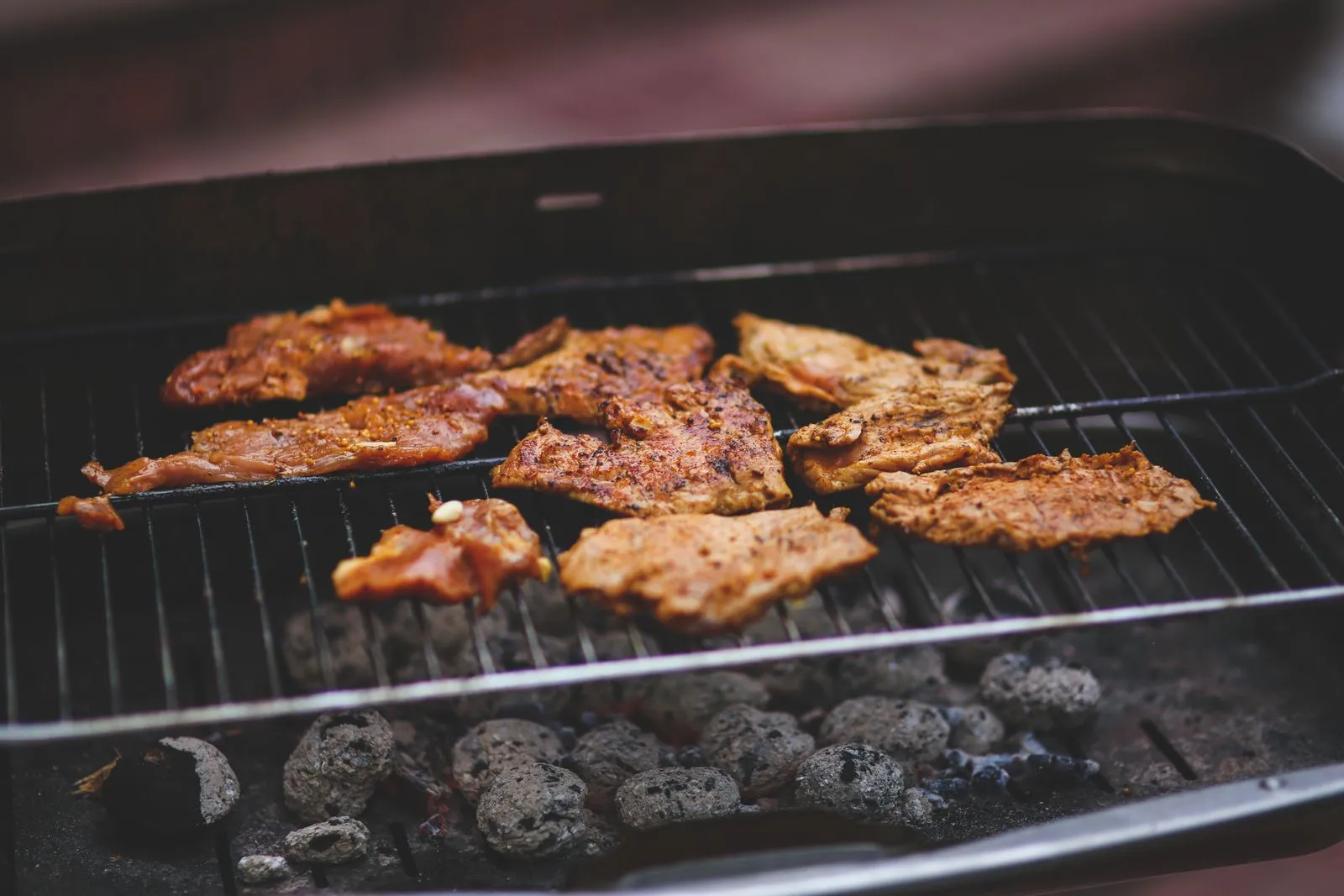 Delicious marinated meats sizzling on a charcoal barbecue grill, perfect for outdoor summer cooking.